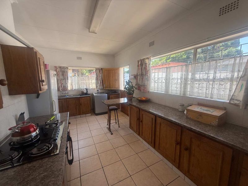 A functional kitchen featuring wooden cabinetry, laminate countertops, a gas hob, and tiled flooring with ample natural light from large windows.