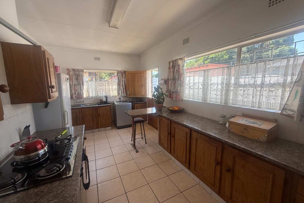 A functional kitchen featuring wooden cabinetry, laminate countertops, a gas hob, and tiled flooring with ample natural light from large windows.