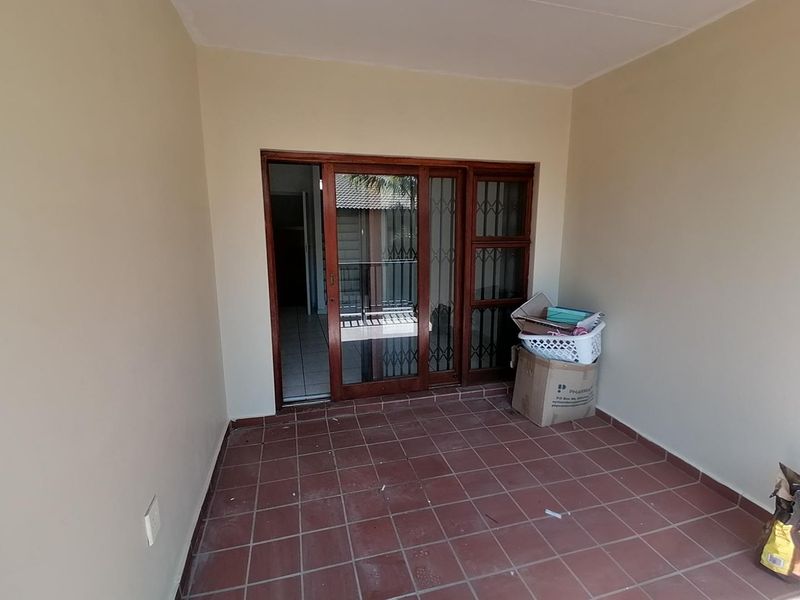 A covered patio area featuring tiled flooring and a sliding glass door with an integrated security gate.