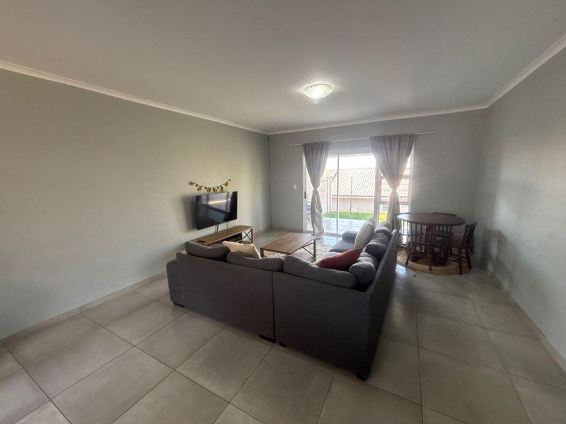 A spacious living room featuring neutral tiled flooring, coved cornicing, and a sliding glass door providing access to the rear patio area.