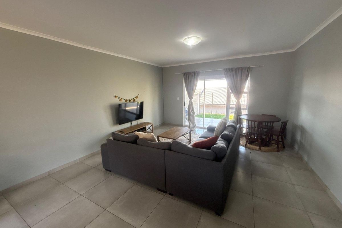 A spacious living room featuring neutral tiled flooring, coved cornicing, and a sliding glass door providing access to the rear patio area.