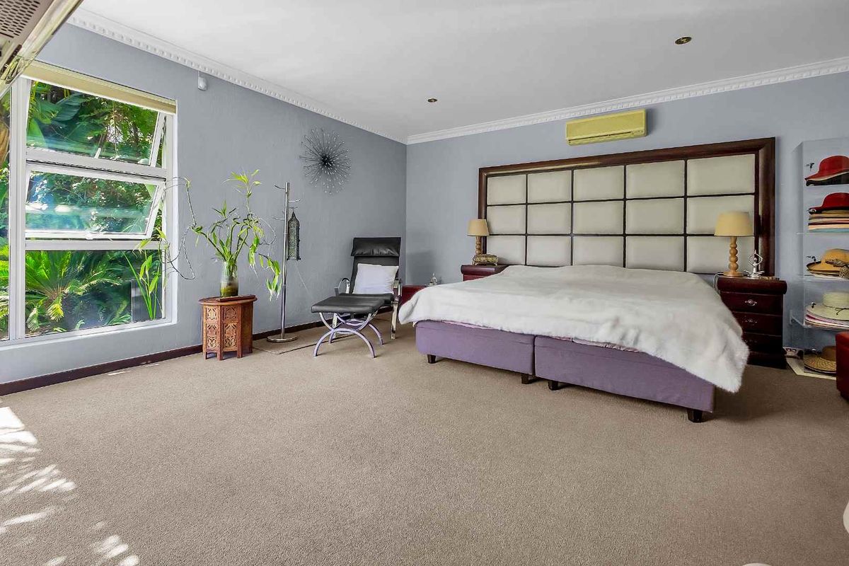 Spacious bedroom featuring neutral carpeting, crown molding, and a large window providing natural light and garden views.