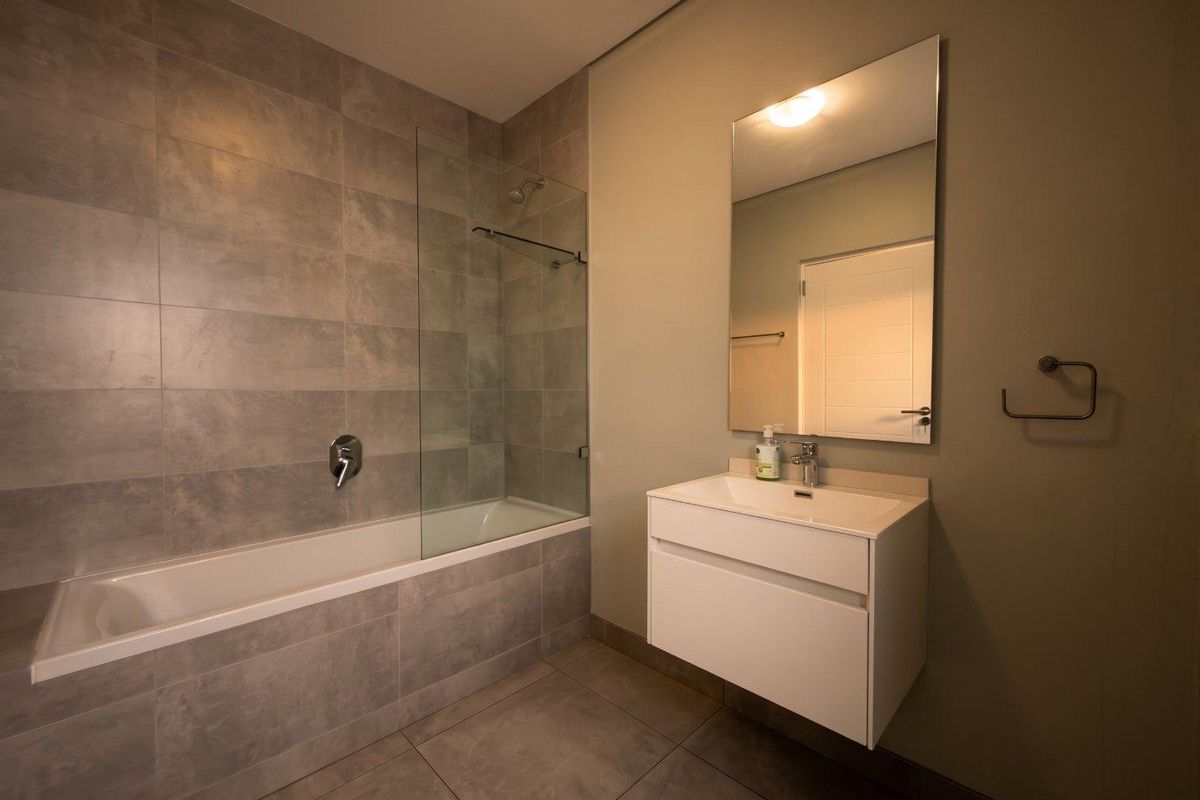 Modern bathroom featuring a wall-mounted vanity with integrated basin, a bathtub with a glass shower screen, and neutral grey tiled finishes.