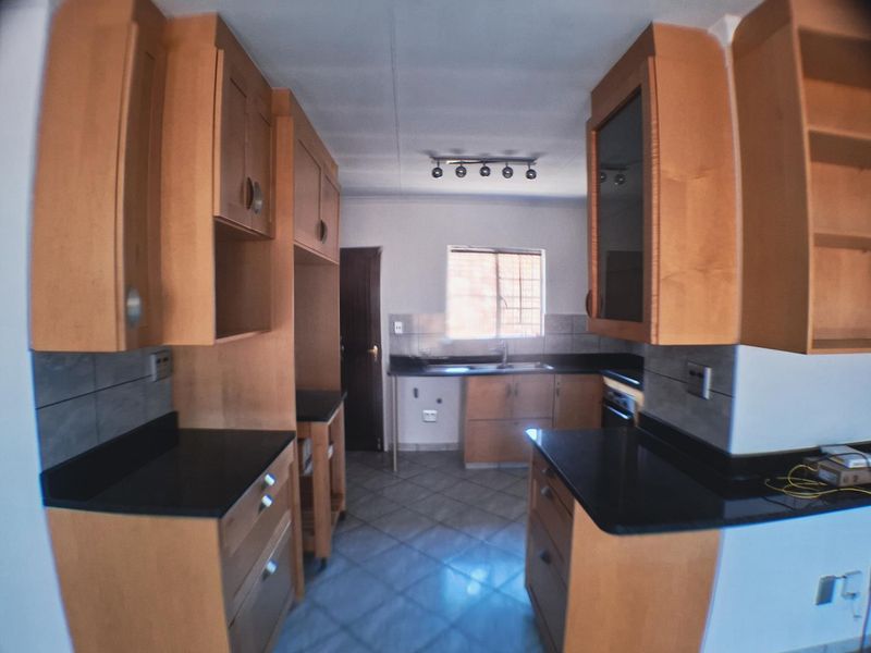 A functional kitchen featuring wooden cabinetry, dark stone countertops, tiled flooring, and a tiled backsplash, offering a clean and practical workspace.