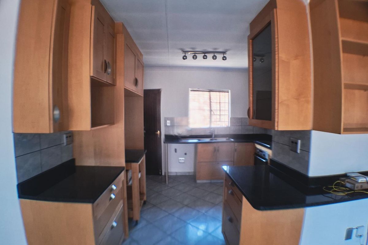 A functional kitchen featuring wooden cabinetry, dark stone countertops, tiled flooring, and a tiled backsplash, offering a clean and practical workspace.