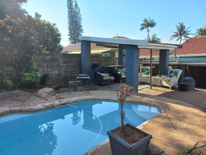Outdoor pool area featuring a swimming pool, paved surround, and a covered patio structure with a built-in braai area.