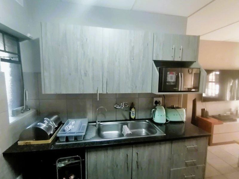 A compact kitchen featuring wood-look cabinetry, a stainless steel sink, tiled backsplash, and a built-in microwave.
