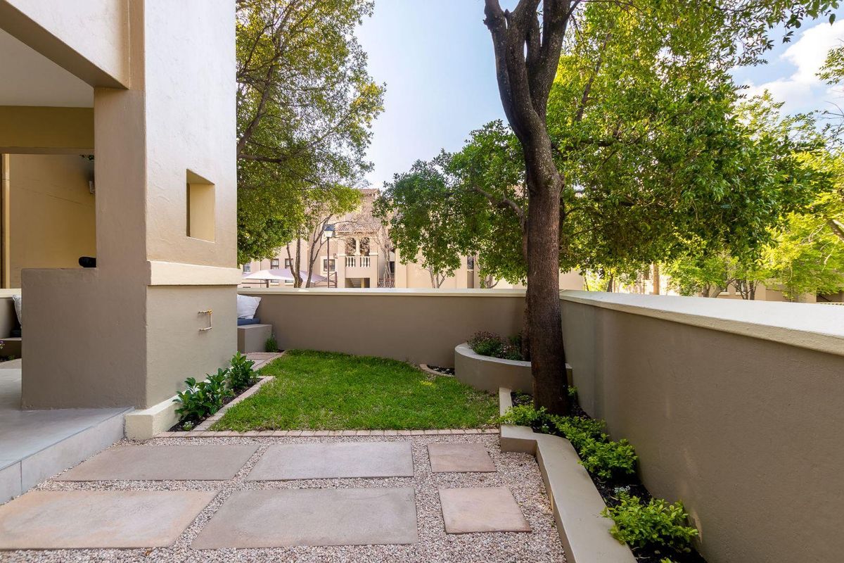 A well-maintained private rear garden featuring a paved patio area, lawn, and built-in planter boxes with established trees.