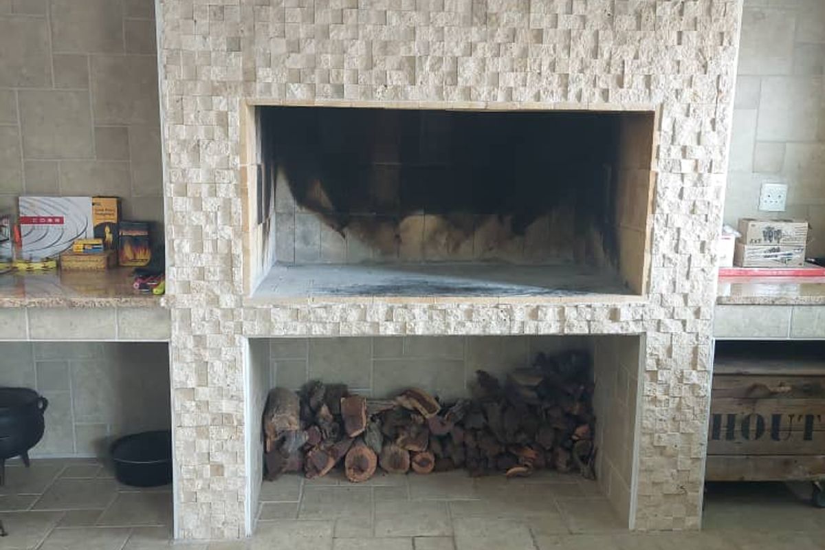 A built-in indoor braai or fireplace featuring textured stone cladding, integrated side counters, and a dedicated lower storage compartment for firewood.