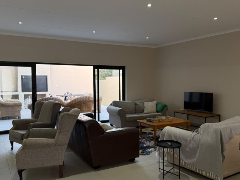 Spacious living room featuring neutral tiled flooring, recessed downlighting, and large sliding glass doors providing seamless access to the outdoor patio area.