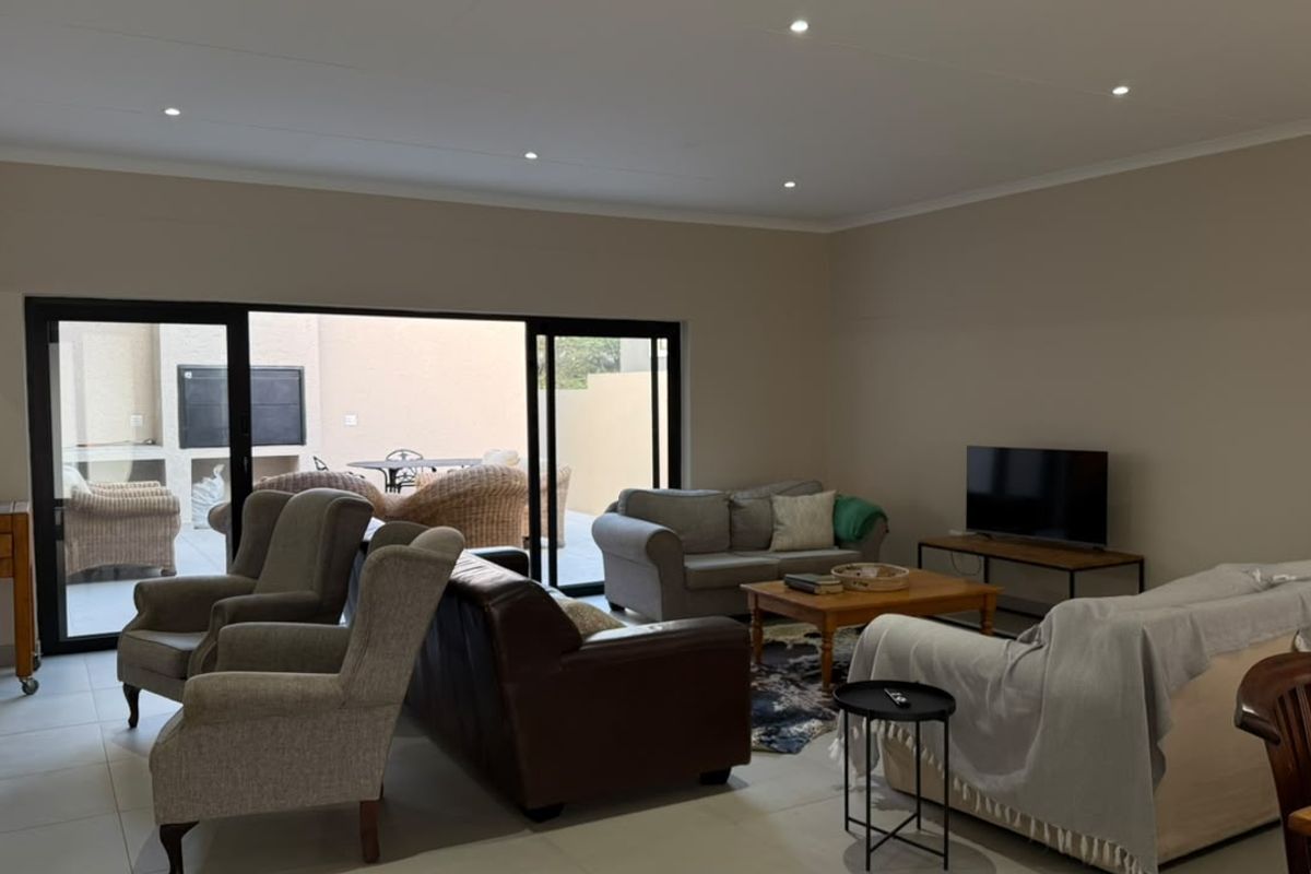 Spacious living room featuring neutral tiled flooring, recessed downlighting, and large sliding glass doors providing seamless access to the outdoor patio area.