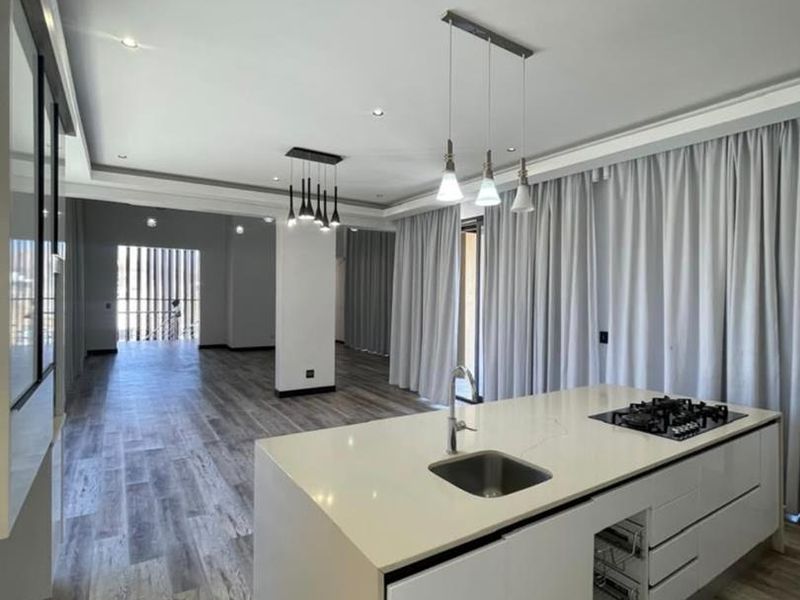 Modern open-plan living area featuring a sleek kitchen island with integrated gas hob, recessed lighting, and wood-look laminate flooring throughout.