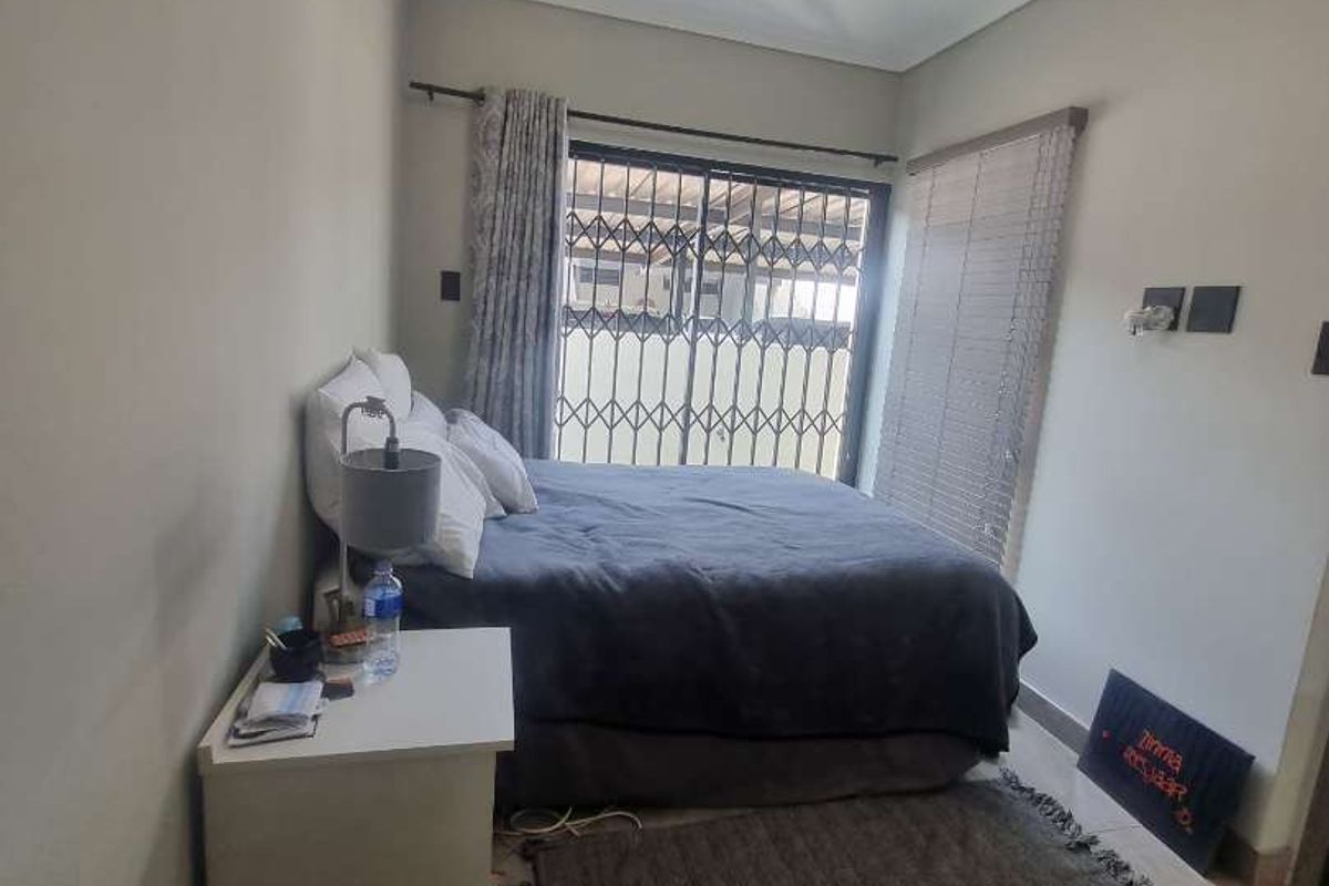 A functional bedroom featuring tiled flooring, a security gate on the window, and neutral wall finishes.