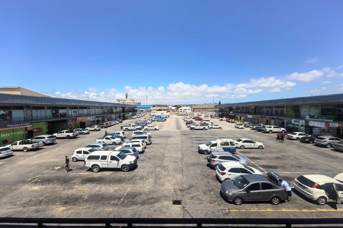 An elevated view of a commercial parking lot flanked by two rows of retail storefronts with metal roof structures.