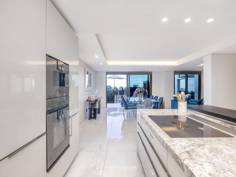 Modern open-plan kitchen and living area featuring high-end finishes, stone island with integrated cooktop, and seamless flow to an outdoor balcony.