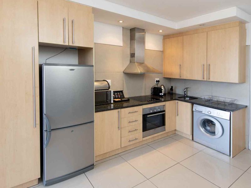 Modern kitchen featuring light-wood cabinetry, granite countertops, integrated stainless steel appliances, and neutral tiled flooring.