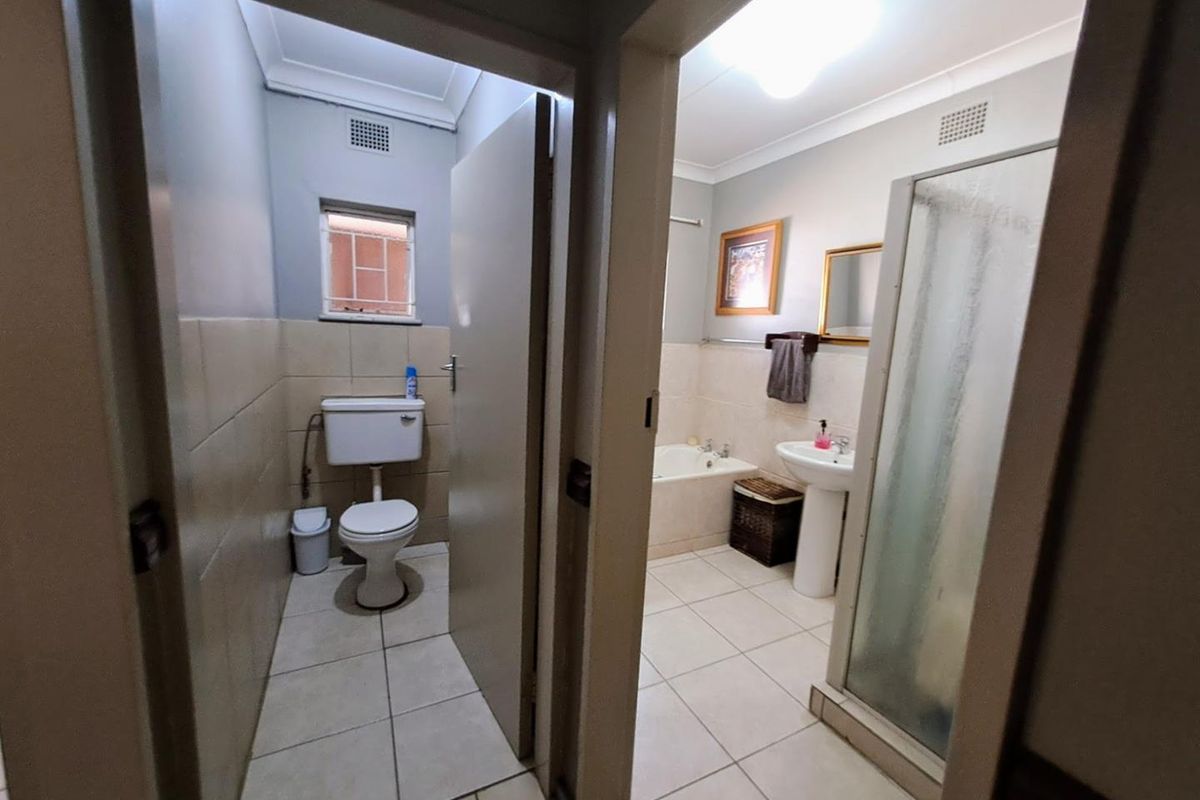 A functional bathroom featuring a separate toilet area, a pedestal basin, a bathtub, and a glass-enclosed shower with neutral floor and wall tiling.
