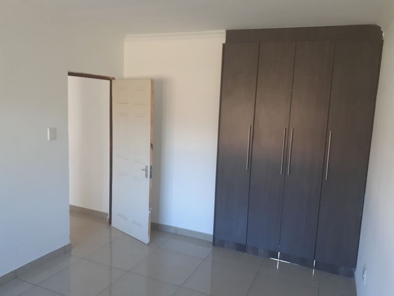 A vacant bedroom featuring tiled flooring and dark wood-finish built-in cupboards, providing a clean and neutral space ready for personalization.