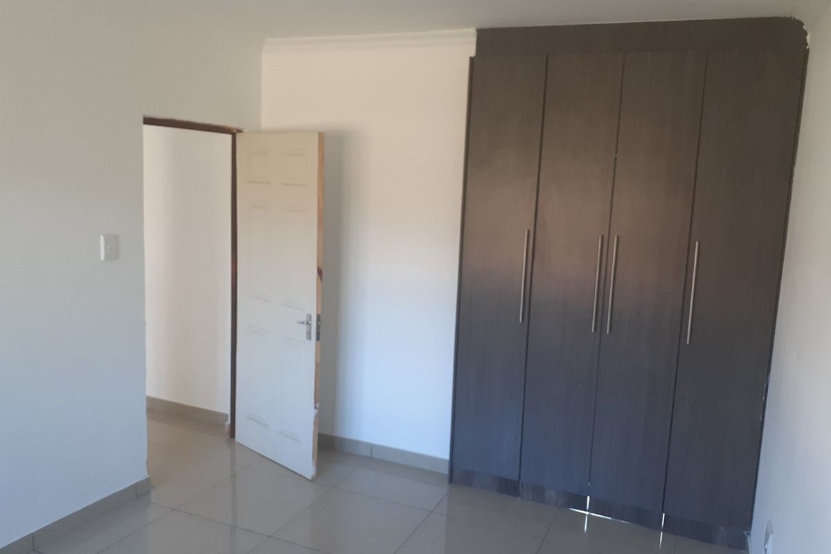 A vacant bedroom featuring tiled flooring and dark wood-finish built-in cupboards, providing a clean and neutral space ready for personalization.