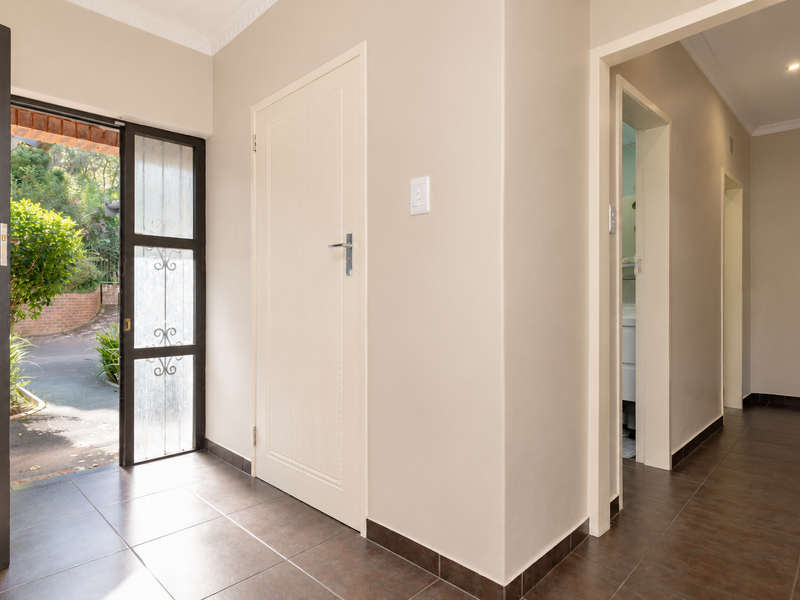 A bright entrance foyer featuring tiled flooring, coved cornicing, and direct access to the exterior through a security gate.