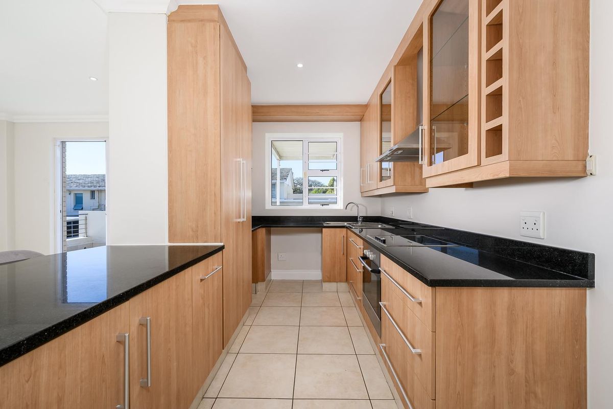 A modern, well-maintained kitchen featuring light wood cabinetry, contrasting black granite countertops, integrated appliances, and tiled flooring.