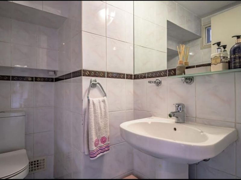 A functional bathroom featuring a pedestal basin, toilet, and fully tiled walls with a decorative border.