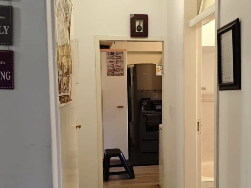 A view through a hallway connecting to a kitchen and bathroom area, featuring standard door frames and laminate flooring.