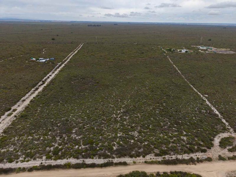 An aerial view of a large, undeveloped agricultural land parcel featuring natural vegetation, perimeter fencing, and access roads.