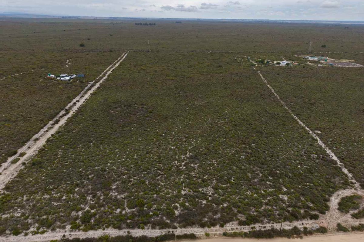 An aerial view of a large, undeveloped agricultural land parcel featuring natural vegetation, perimeter fencing, and access roads.