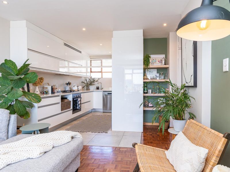 Modern open-plan kitchen featuring sleek white cabinetry, built-in appliances, and a seamless transition between tiled kitchen area and warm parquet wood flooring.