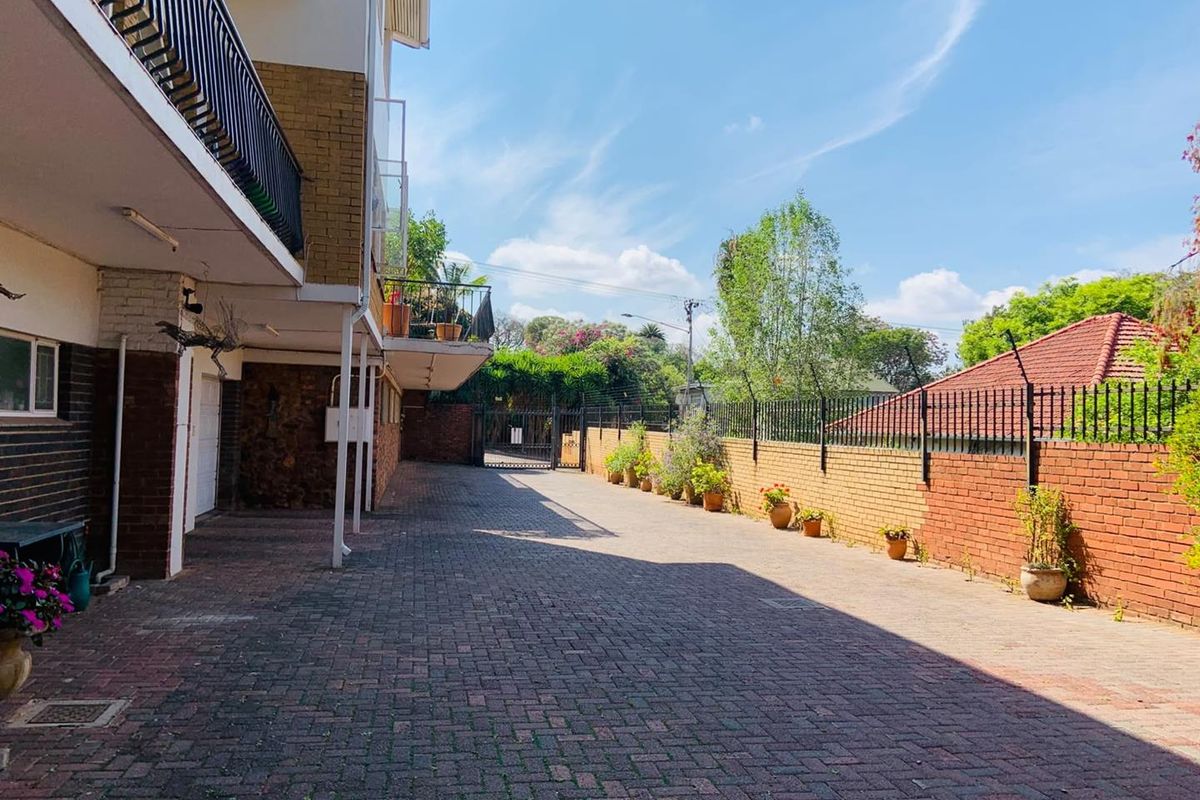 A paved rear courtyard area featuring brick boundary walls with security fencing and access to the apartment building's lower level and balconies.