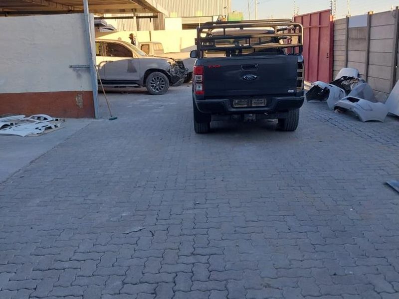 Industrial rear yard area featuring paved surfacing, a covered parking structure, and perimeter walling with electric fencing.