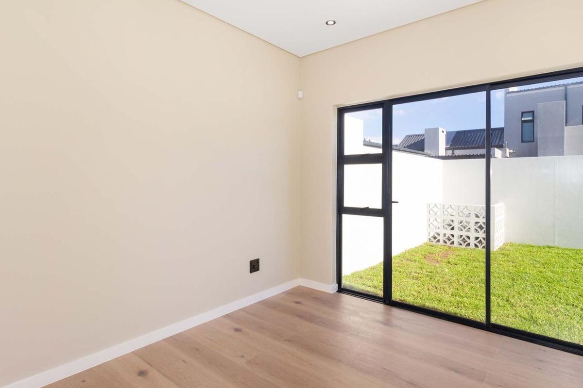 A bright, modern bedroom featuring light wood-look flooring, neutral walls, and large sliding glass doors providing direct access to a private rear garden.