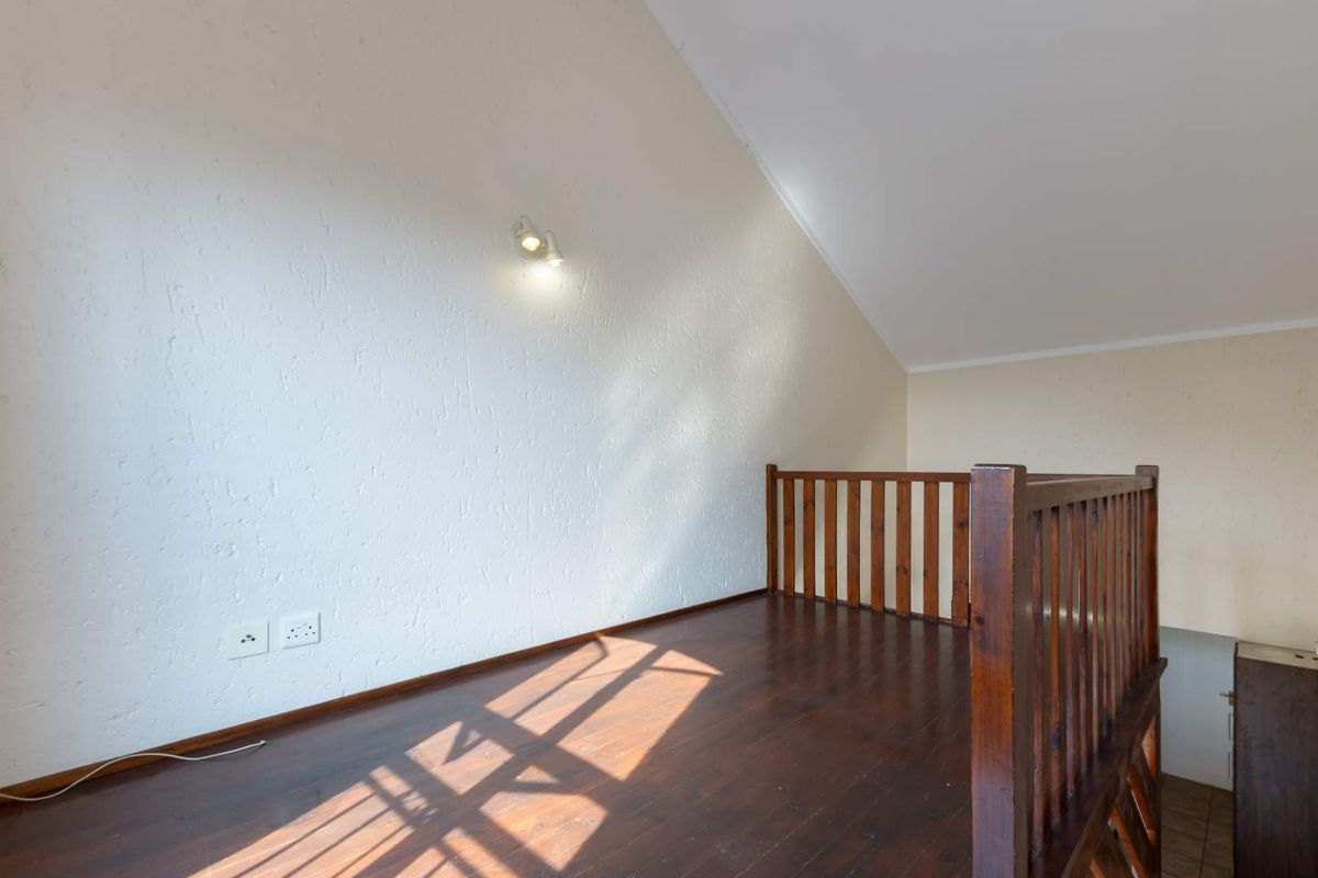 A loft-style mezzanine area featuring dark wooden flooring, a timber balustrade, and a vaulted ceiling with wall-mounted lighting.
