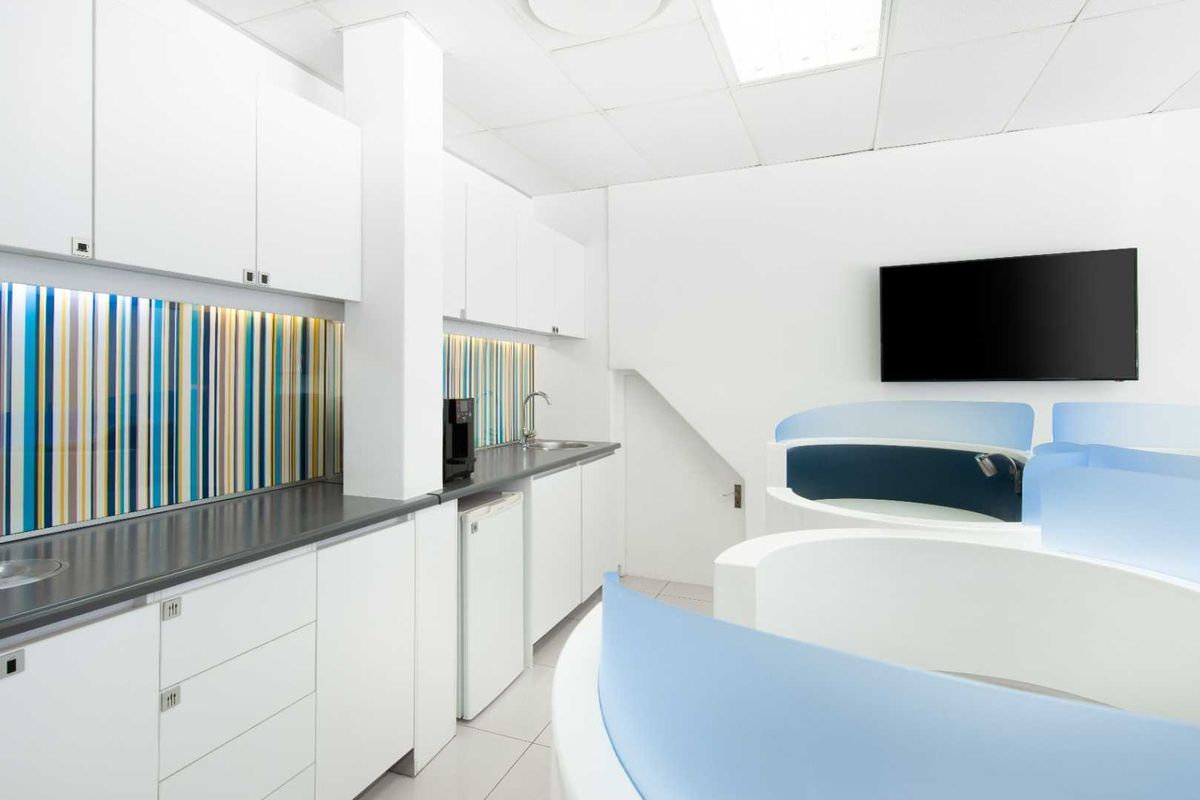 Modern office kitchenette featuring white cabinetry, dark countertops, a stainless steel sink, and a vibrant striped glass backsplash.
