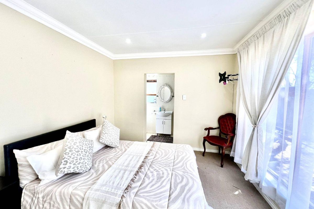 A bedroom featuring neutral walls, carpeted flooring, and an en-suite bathroom with a vanity unit, leading to an outdoor area via sliding glass doors.