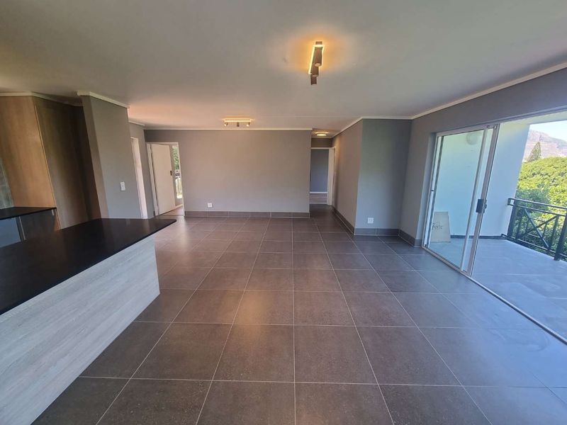 Spacious open-plan living area featuring modern tiled flooring, a kitchen island with stone countertop, and large sliding doors leading to a balcony.