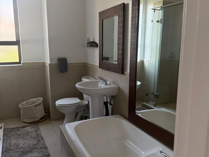 A well-maintained bathroom featuring a pedestal basin, built-in bathtub, toilet, and a separate glass-enclosed shower with neutral tiled finishes.