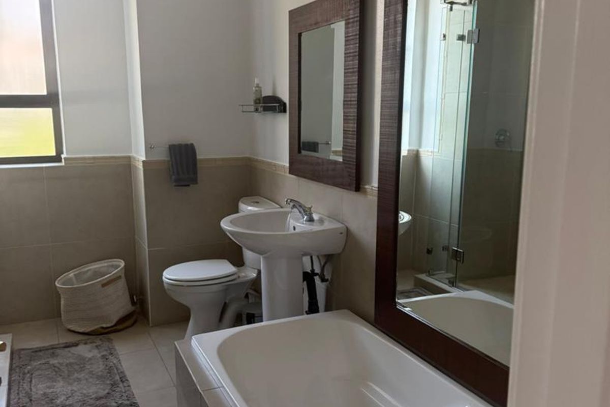 A well-maintained bathroom featuring a pedestal basin, built-in bathtub, toilet, and a separate glass-enclosed shower with neutral tiled finishes.