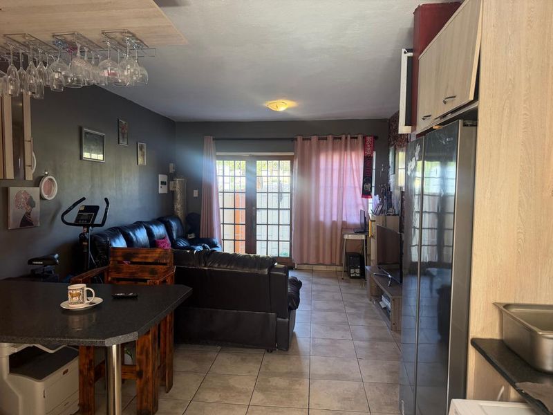Open plan living area featuring tiled flooring and glass paneled doors leading to the exterior, seamlessly connected to a functional kitchen space.