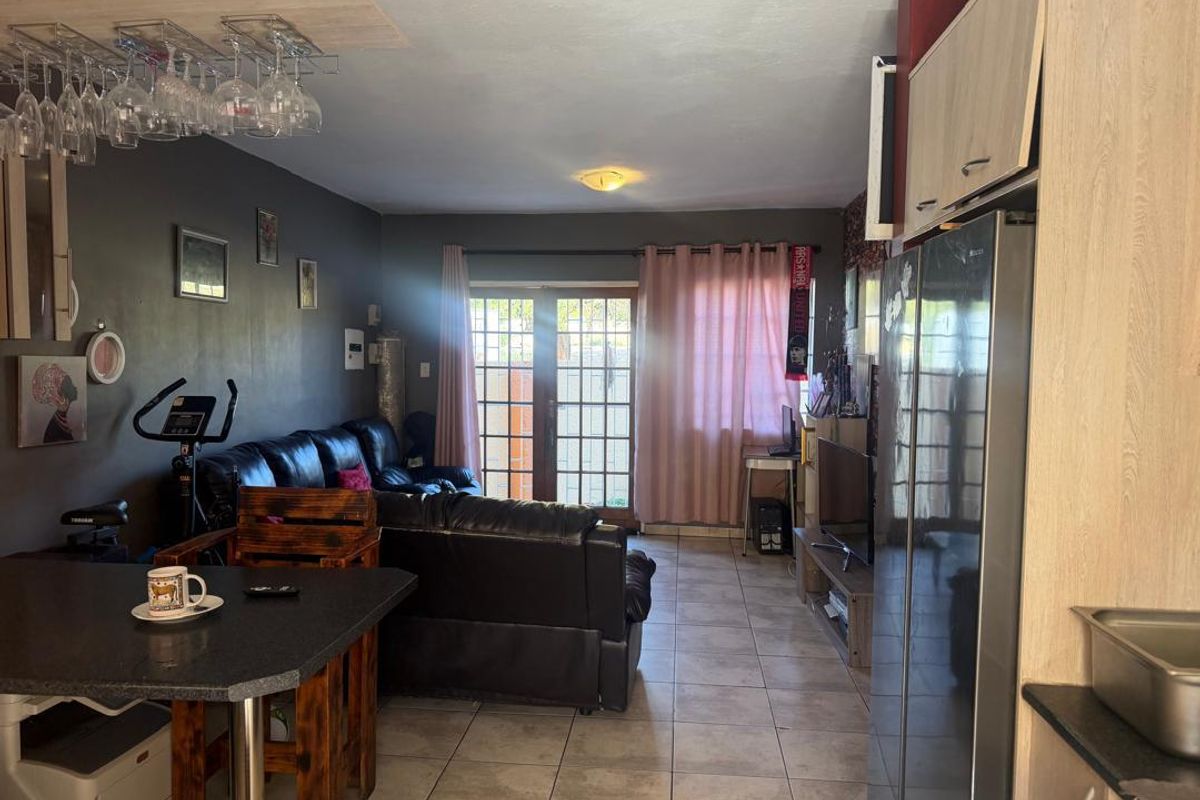 Open plan living area featuring tiled flooring and glass paneled doors leading to the exterior, seamlessly connected to a functional kitchen space.