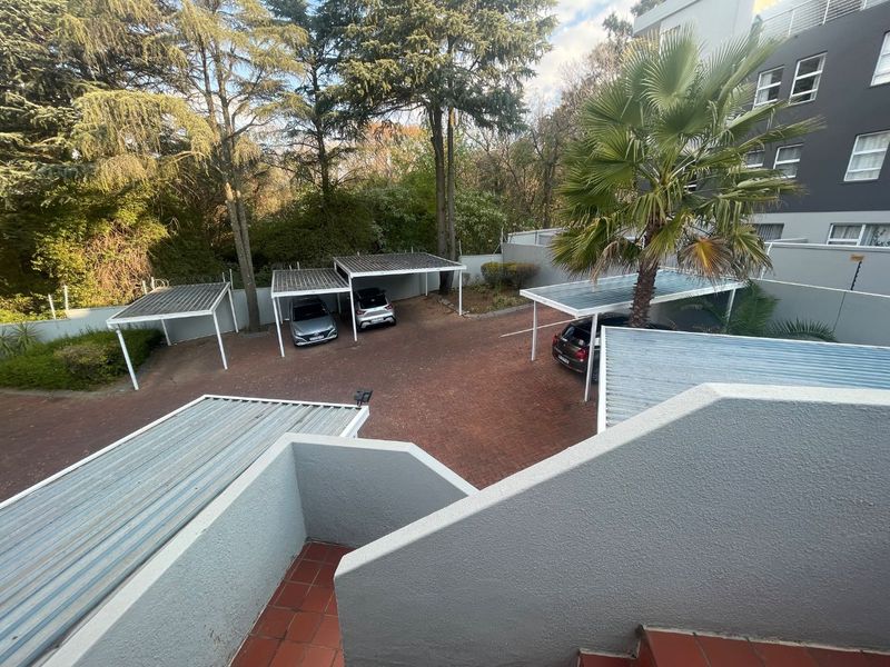 An elevated view of the apartment complex rear area featuring paved parking bays with carports and surrounding perimeter walls.