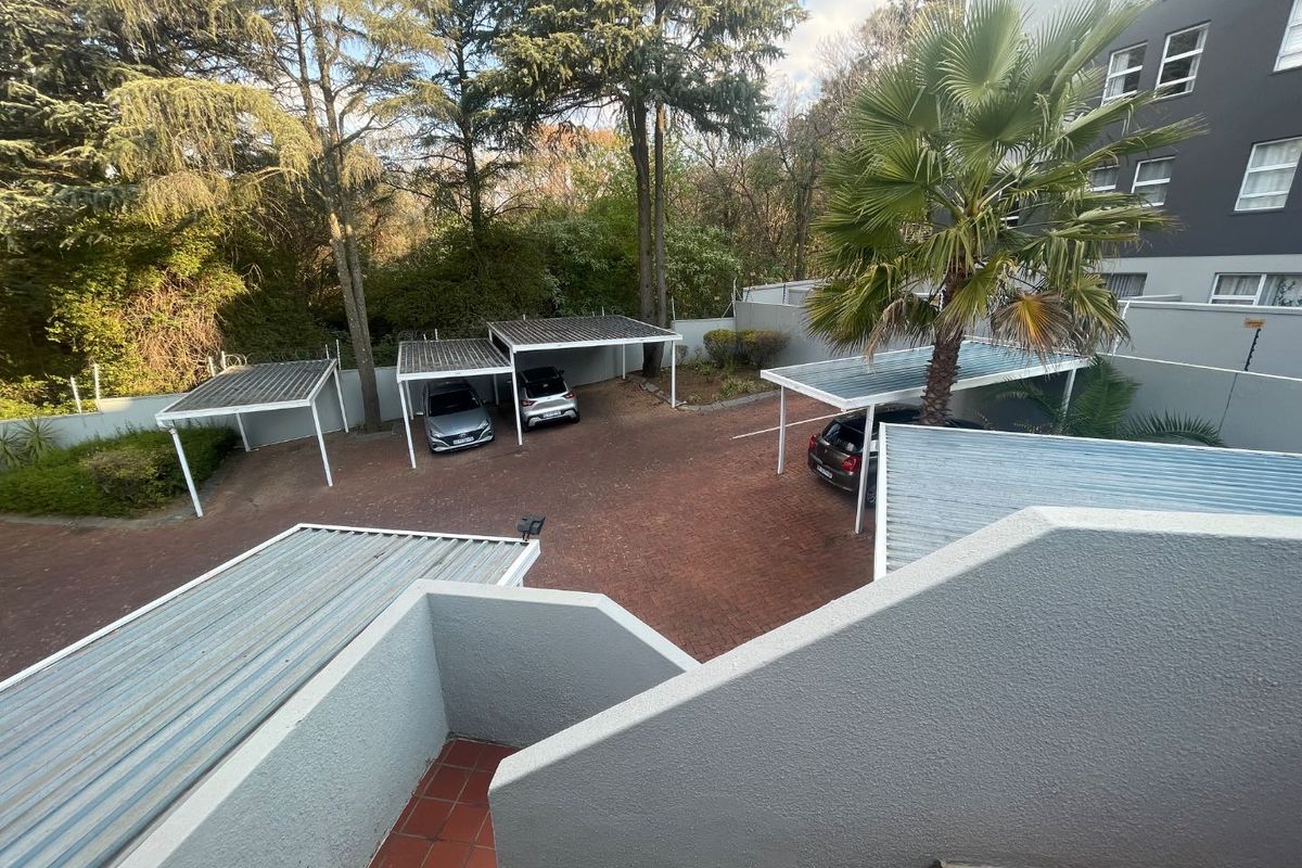 An elevated view of the apartment complex rear area featuring paved parking bays with carports and surrounding perimeter walls.