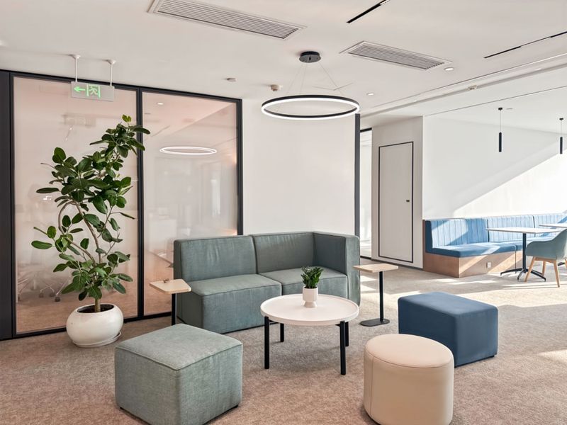 Modern office breakout area featuring glass partitions, recessed ceiling lighting, and integrated bench seating in a professional, well-maintained workspace.