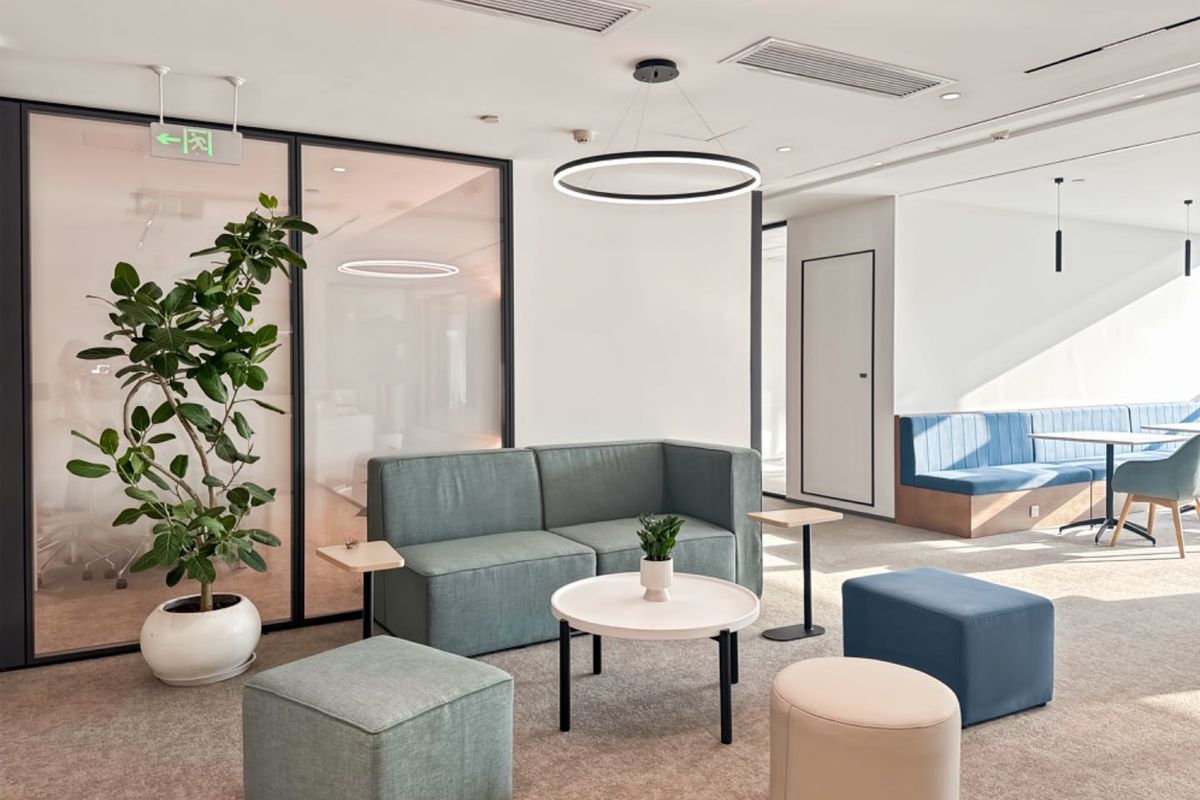 Modern office breakout area featuring glass partitions, recessed ceiling lighting, and integrated bench seating in a professional, well-maintained workspace.