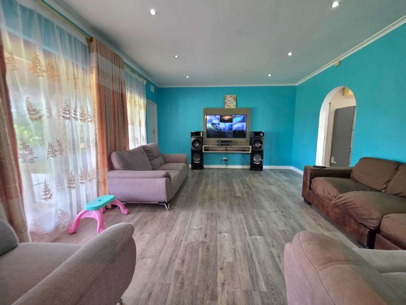 Spacious living room featuring modern wood-look laminate flooring, recessed downlighting, and a built-in media console wall unit.