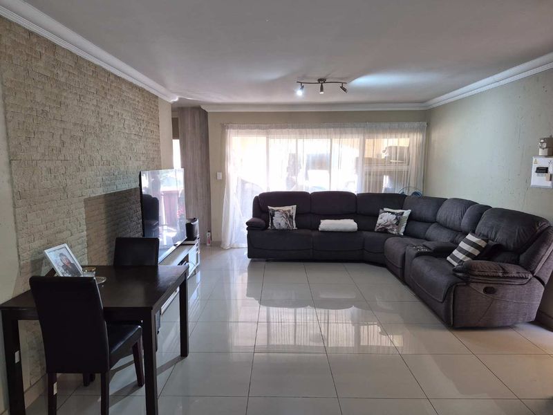 Spacious living room featuring a textured stone accent wall, polished tiled flooring, and ceiling coving, providing a comfortable and well-maintained living space.