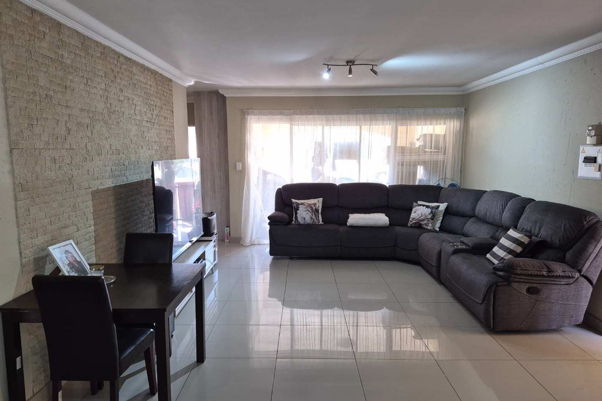 Spacious living room featuring a textured stone accent wall, polished tiled flooring, and ceiling coving, providing a comfortable and well-maintained living space.