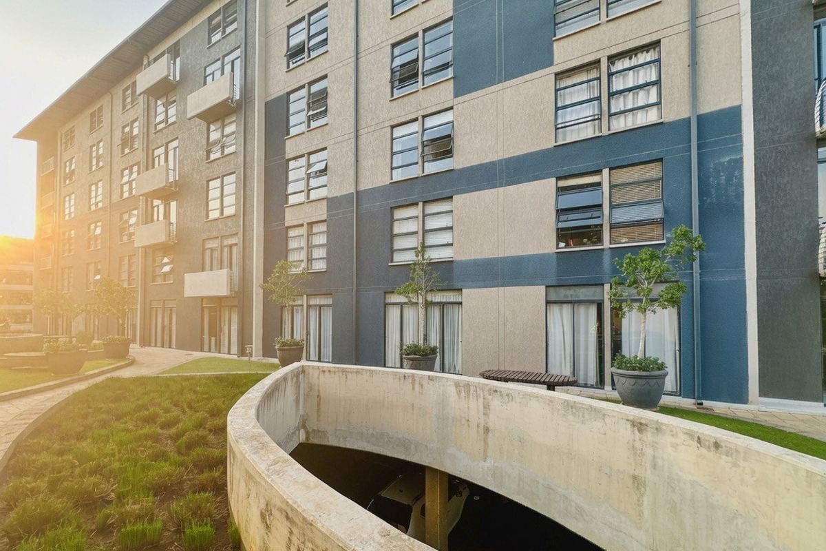 Exterior view of a modern multi-story apartment building featuring balconies, a landscaped garden area, and a concrete ramp leading to underground parking.
