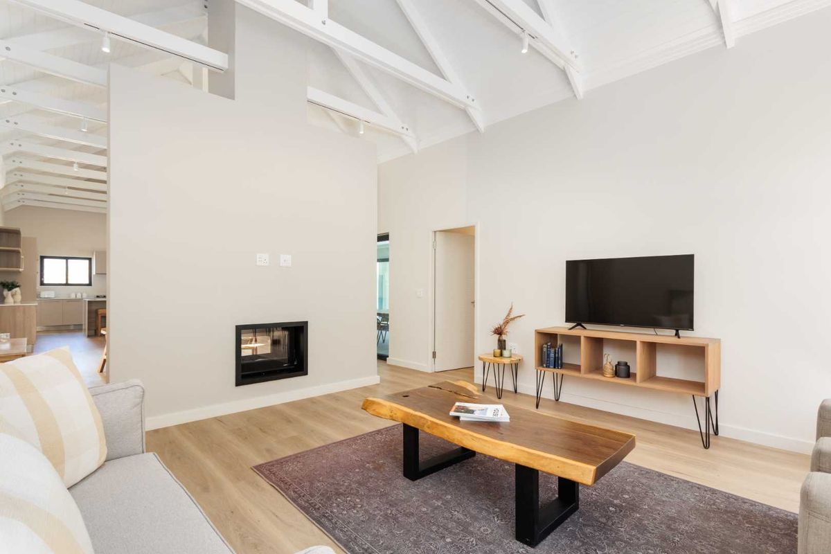 Bright and airy living room featuring a vaulted ceiling with exposed rafters, modern laminate flooring, and a sleek built-in fireplace.